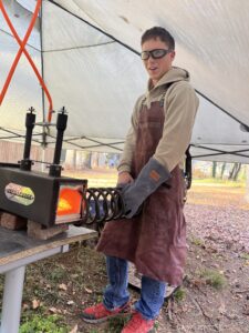 Elian Pope wearing safety glasses and a protective apron beside his forge.