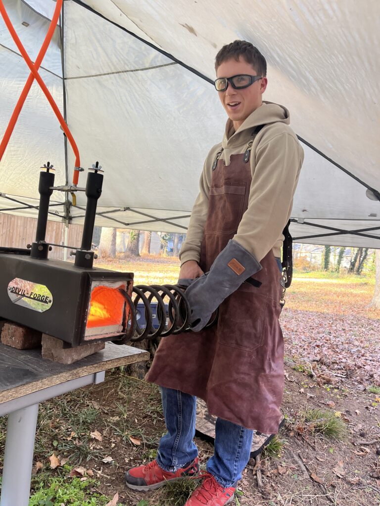 Elian Pope wearing safety glasses and a protective apron beside his forge.
