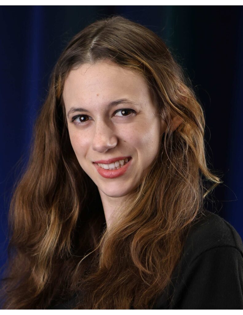 Isabella Grbac smiling in a headshot against a dark background.